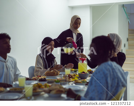 A diverse Islamic family gathers for iftar, joyfully breaking their fast together during Ramadan, with a Muslim woman in a beautiful hijab gracefully pouring water to mark the end of their fast 121337212