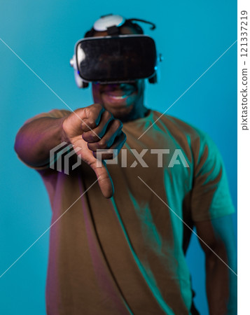 African American man, wearing virtual reality glasses, expresses dissatisfaction by pointing down with his hand while standing isolated against a blue background, portraying a modern critique within 121337219