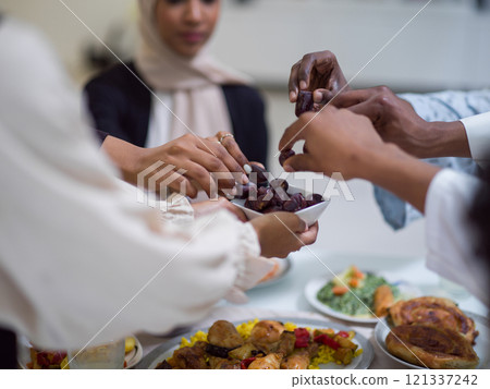 A woman in a hijab extends a platter of dates to her diverse family, creating a scene of unity and joy as they come together to break their fast during the holy month of Ramadan, symbolizing the 121337242