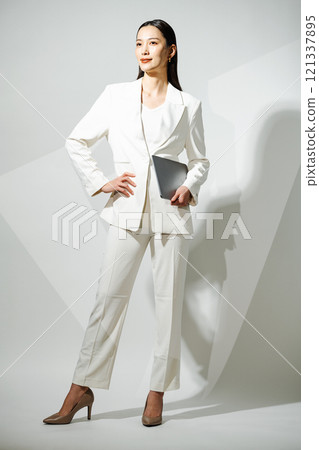 A tall career woman wearing a white pantsuit and holding a laptop A tall career woman wearing a white pantsuit and holding a laptop 121337895