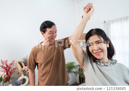 Joyful Retired Couple Dancing Together in Their Cozy Living Room, Embracing Life and Happiness in a Warm and Inviting Home Setting 121338085