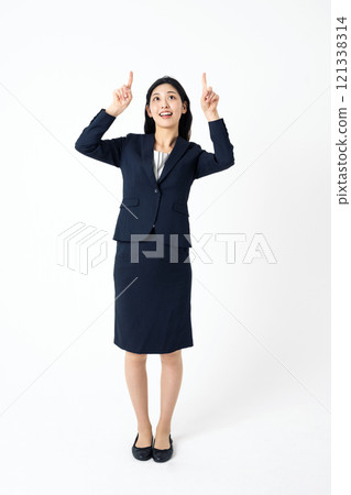 Full-body portrait of a young woman in a suit pointing straight up 121338314