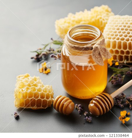 jar of golden honey with wooden dipper, surrounded by honeycomb and flowers, creates natural and rustic setting. honey rich color and texture are highlighted against dark background jar of golden honey with wooden dipper, surrounded by honeycomb and flowers, creates natural and rustic setting. honey rich color and texture are highlighted against dark background 121338464