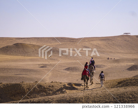 A group of people riding camels in a desert 121338966