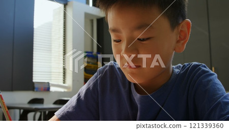 Front view of attentive Asian schoolboy studying at desk in classroom at school 121339360