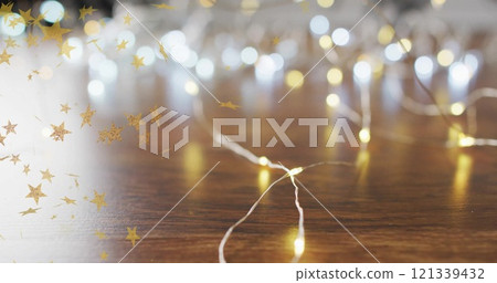 Golden stars image over string lights on wooden surface 121339432