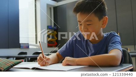 Front view of attentive Asian schoolboy studying at desk in classroom at school 121339440