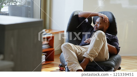 Front view of African american man relaxing on chair in a comfortable home Front view of African american man relaxing on chair in a comfortable home 121339451