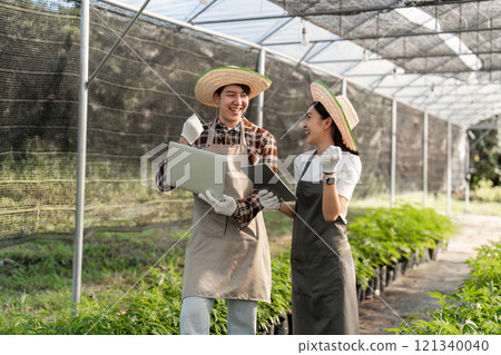 Couple Cultivating an Herbal Garden with Modern Technology in a Greenhouse Setting 121340040