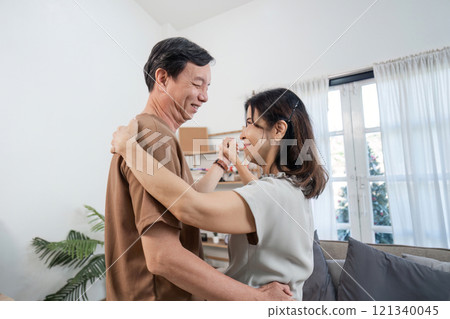 Joyful Retired Couple Dancing Together in Their Cozy Living Room, Embracing Happiness and Love in Their Golden Years 121340045