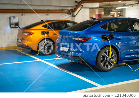 Two electric cars are charging in a well lit parking garage at the shopping mall Two electric cars are charging in a well lit parking garage at the shopping mall 121340306