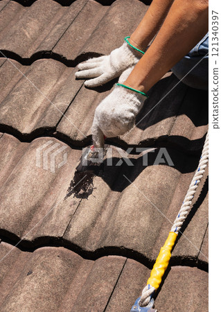 Worker man using waterproof roof coating repair to fix crack of the old tile roof. 121340397