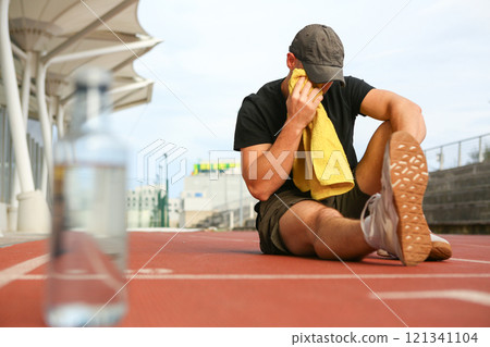 Man sitting on athletics track drying himself with towel after playing sports 121341104