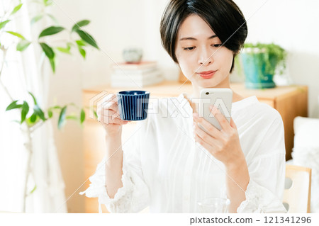 年輕女子一邊吃飯一邊看智慧型手機 121341296