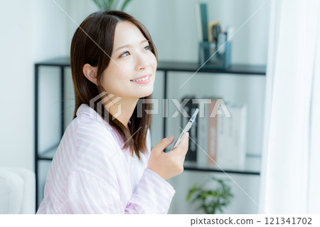 A young woman operating a smartphone in a room 121341702