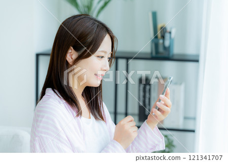 在房間裡操作智慧型手機的年輕女子 在房間裡操作智慧型手機的年輕女子 121341707