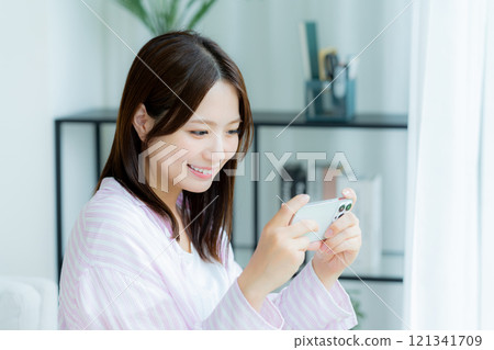 A young woman operating a smartphone in a room A young woman operating a smartphone in a room 121341709