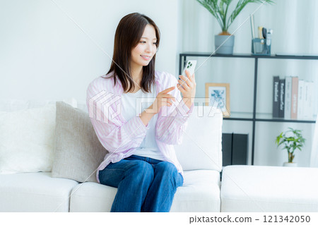 A young woman operating a smartphone in a room 121342050