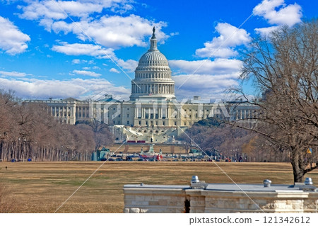The US Capitol as seen from the National Mall surrounded by bare trees under a clear blue sky in Washington DC 121342612