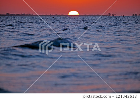 Breathtaking ocean sunset with vivid orange sky, gentle waves, and serene beach shoreline 121342618