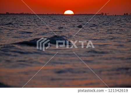 Breathtaking ocean sunset with vivid orange sky, gentle waves, and serene beach shoreline 121342619