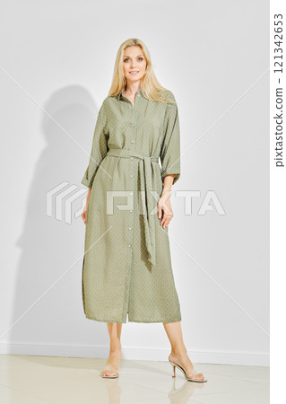 Beautiful woman posing in a green patterned maxi dress with high heels on a white background 121342653