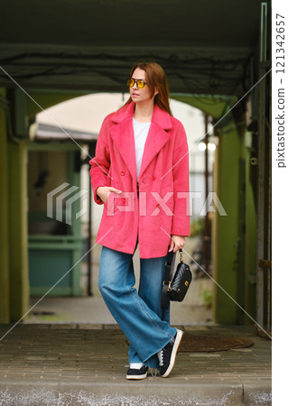 A woman in a bright pink coat and sunglasses waiting for taxi in a colorful urban setting A woman in a bright pink coat and sunglasses waiting for taxi in a colorful urban setting 121342657