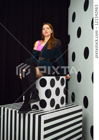 Stylish woman poses on geometric display in trendy indoor setting Stylish woman poses on geometric display in trendy indoor setting 121342663