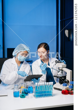 Young scientists conducting research investigations in a medical laboratory, a researcher in the foreground is using a microscope in laboratory Young scientists conducting research investigations in a medical laboratory, a researcher in the foreground is using a microscope in laboratory 121342953