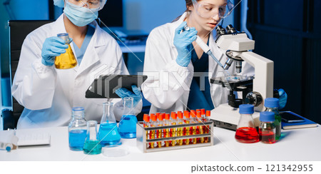 Young scientists conducting research investigations in a medical laboratory, a researcher in the foreground is using a microscope in laboratory Young scientists conducting research investigations in a medical laboratory, a researcher in the foreground is using a microscope in laboratory 121342955