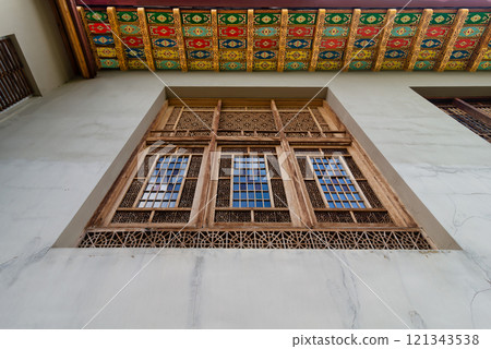 Intricate wooden window at the Shakikhanovs Palace in Shaki, Azerbaijan, framed by a colorful, patterned ceiling 121343538