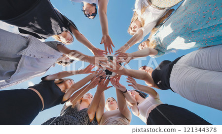 Group of high school girls forming a circle, holding a soccer ball together, symbolizing teamwork and unity under a clear blue sky 121344378