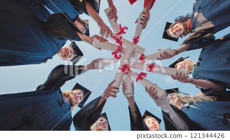 Group of young people wearing academic gowns and caps celebrating graduation by holding their diplomas together. Group of young people wearing academic gowns and caps celebrating graduation by holding their diplomas together. 121344426