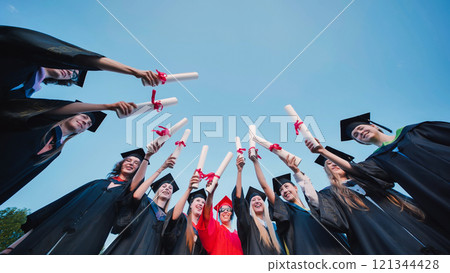 Happy students in academic gowns and graduation caps raising their diplomas in celebration of their graduation Happy students in academic gowns and graduation caps raising their diplomas in celebration of their graduation 121344428