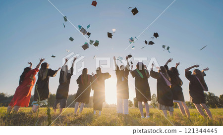 Students jubilantly tossing their graduation caps into the air in front of a breathtaking sunset 121344445