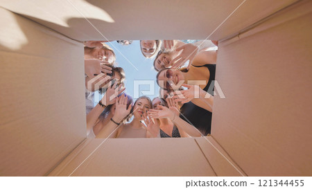 Cheerful high school students waving from inside a cardboard box, enjoying their summer break together Cheerful high school students waving from inside a cardboard box, enjoying their summer break together 121344455