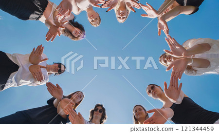 High school students joining hands in a circle under a clear blue sky, representing teamwork and solidarity High school students joining hands in a circle under a clear blue sky, representing teamwork and solidarity 121344459
