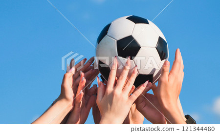 Pedicured female hands lift and twirl a soccer ball against a blue sky. 121344480