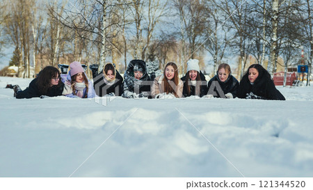 Group of smiling schoolgirls lying on their stomachs in the snow, enjoying winter in a snowy park Group of smiling schoolgirls lying on their stomachs in the snow, enjoying winter in a snowy park 121344520