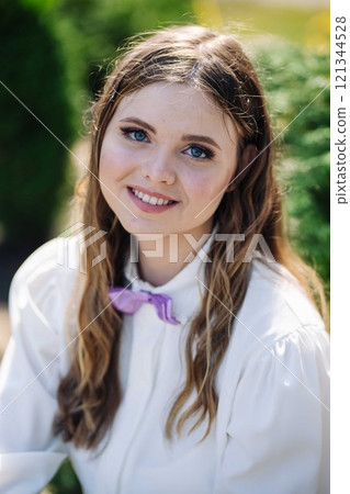 Happy schoolgirl in white shirt and purple bow tie smiles on her first day of school in portrait 121344528