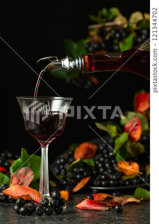 Black chokeberry liqueur is poured from a bottle into a glass. Black chokeberry liqueur is poured from a bottle into a glass. 121344702