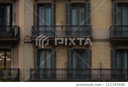 Traditional Barcelona facade with symmetrical windows, green shutters, and ornate black iron balconies. 121345486