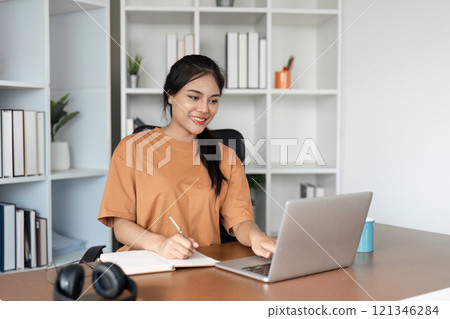Young Girl Studying Online from Home with Laptop and Notebook in Modern Home Office Setting Young Girl Studying Online from Home with Laptop and Notebook in Modern Home Office Setting 121346284
