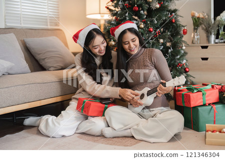 Joyful Young Couple Celebrating Christmas with Gifts and Music by the Tree in a Cozy Living Room Setting 121346304