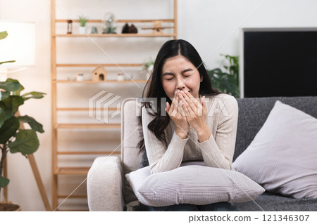 Young Woman Feeling Unwell on Sofa at Home, Sneezing and Covering Mouth, Battling Cold or Flu in Cozy Living Room Setting Young Woman Feeling Unwell on Sofa at Home, Sneezing and Covering Mouth, Battling Cold or Flu in Cozy Living Room Setting 121346307