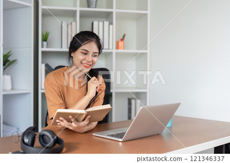 Young Woman Studying Online at Home with Laptop and Notebook, Engaged in E-Learning and Remote Education 121346337