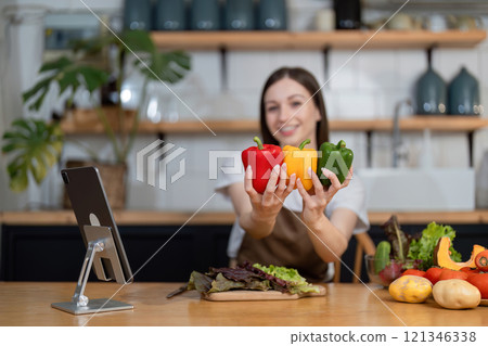 Young Woman Preparing a Healthy Salad with Fresh Vegetables in a Modern Kitchen, Smiling and Holding Bell Peppers 121346338