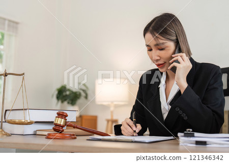 Young Female Lawyer Discussing Business Contract Law Over Phone While Reviewing Documents in Modern Office Young Female Lawyer Discussing Business Contract Law Over Phone While Reviewing Documents in Modern Office 121346342