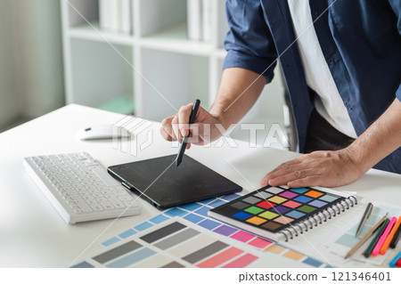 Creative Graphic Designer Planning a Project with Digital Tools and Color Swatches in a Modern Office Environment Creative Graphic Designer Planning a Project with Digital Tools and Color Swatches in a Modern Office Environment 121346401