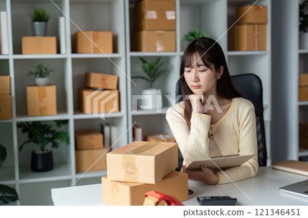 Young Female Entrepreneur Managing Online Sales in a Modern Home Office with Shipping Boxes and Inventory Young Female Entrepreneur Managing Online Sales in a Modern Home Office with Shipping Boxes and Inventory 121346451